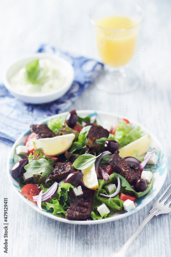 Salad with Grilled Beef Pieces, Cherry Tomatoes, feta Cheese and Kalamata Olives. Bright wooden background. Close up. Salad with Grilled Beef Pieces, Cherry Tomatoes, feta Cheese and Kalamata Olives. Bright wooden background. Close up.