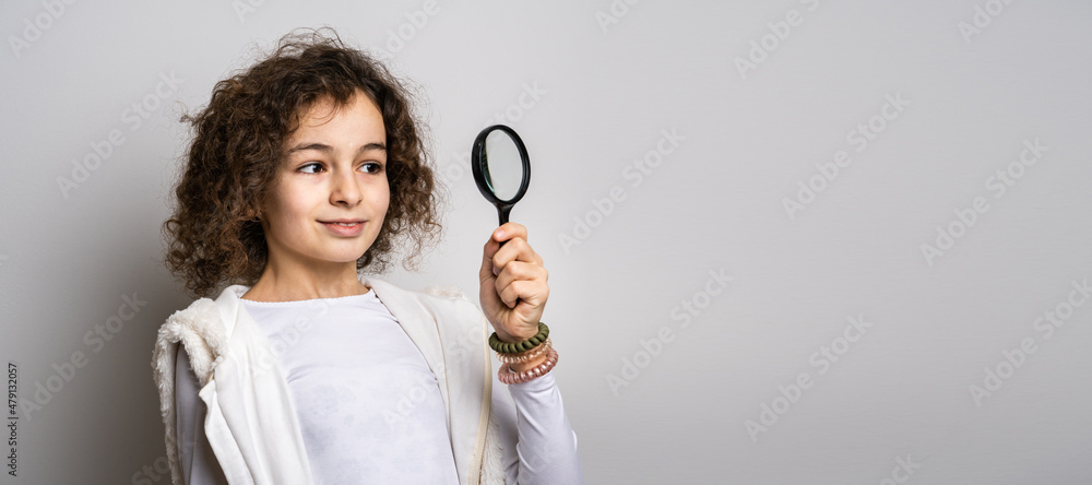 One small caucasian girl ten years old with curly hair front view portrait close up standing in front of white background looking to the camera holding magnifying lens education and learning concept One small caucasian girl ten years old with curly hair front view portrait close up standing in front of white background looking to the camera holding magnifying lens education and learning concept