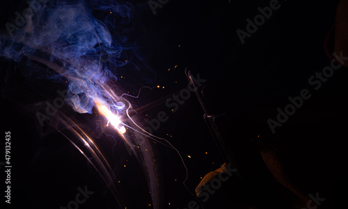 Fototapeta Naklejka Na Ścianę i Meble -  Close-up of a welder working in a workshop. Shallow depth of field. Welding of metal structures. Metal welding. Semi-automatic manual welding. MIG welding.