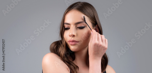 Brunette woman eye with beautiful eyebrows. Perfect shaped brow, eyelashes with brow gel brush. Female model shaping brown eyebrows. Woman portrait isolated on gray studio background.