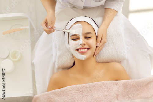Top overhead view beautiful woman or teenage girl with half face covered in calming soothing pampering kaolin clay facial mask for fresh clear skin relaxing on soft towel in beauty parlor or spa salon