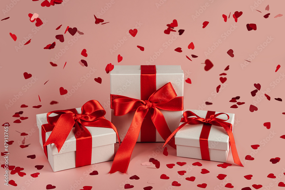 Presents with red bow on rose background with heart confetti. Flat lay style. Valentine day concept. Saint Valentines