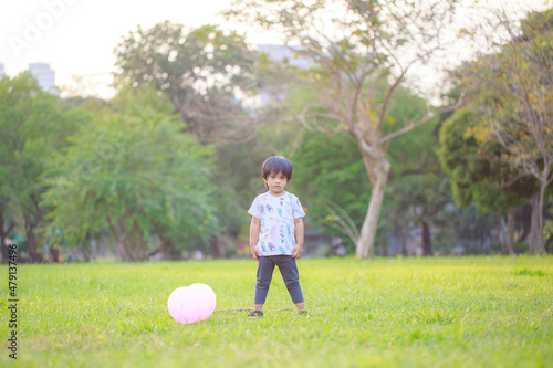 A happy Asian child with colorful toy balloons outside the house. Smiling child having fun in green spring field on blue sky background. freedom concept