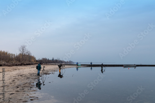 Gruppo di fotografi prima dell'alba sulla spiaggia del mare che fotografano il paesaggio e una piccola barca a motore. photo
