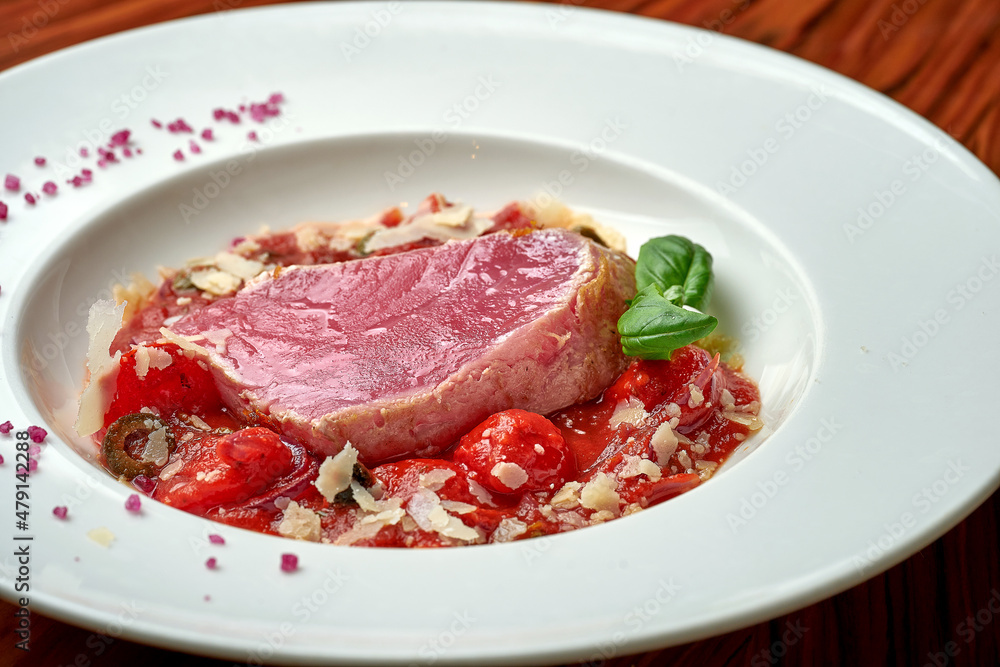 Tuna steak with stewed tomatoes in white plate on wood background Tuna steak with stewed tomatoes in white plate on wood background