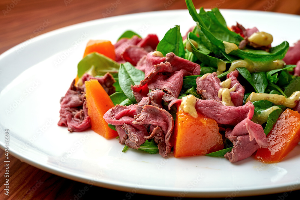 Salad with roast beef and pumpkin in a white plate.