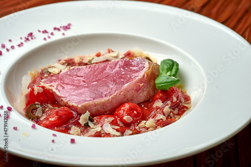 Tuna steak with stewed tomatoes in white plate on wood background