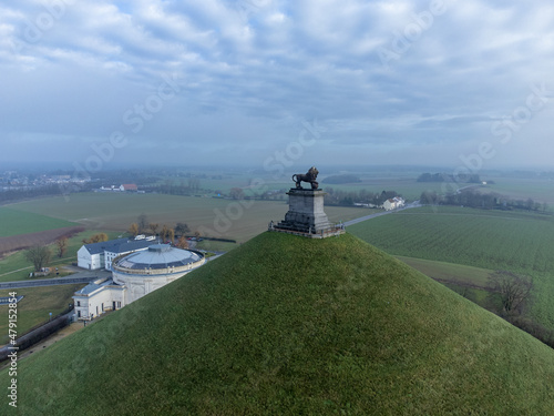  Lion's Mound with farm land and visitor center behind. Dramatic clouds. Butte Du Lion on the battlefield of Waterloo where Napoleon was defeated. Drone aerial view.