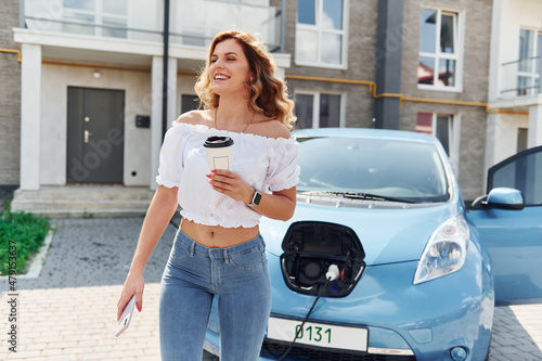 Charging car. Young woman in casual clothes with her electromobile outdoors at daytime © standret