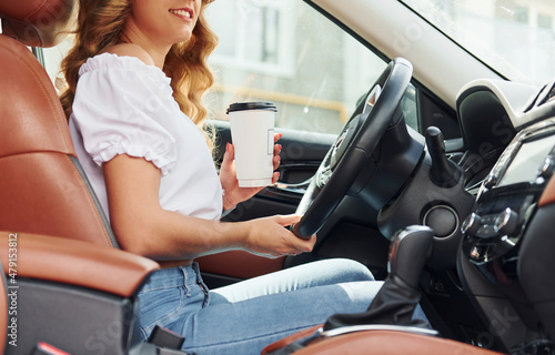 In front of steering wheel. Young woman in casual clothes is sitting in her car at daytime