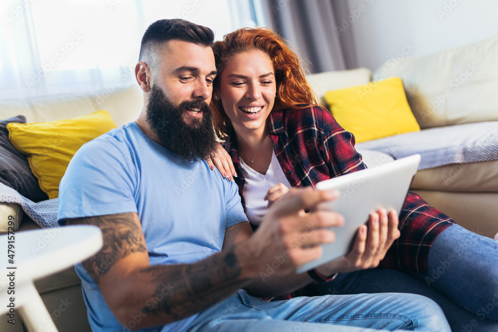 Happy young man and woman spouses relax in living room using modern tablet gadget together. Happy young man and woman spouses relax in living room using modern tablet gadget together.