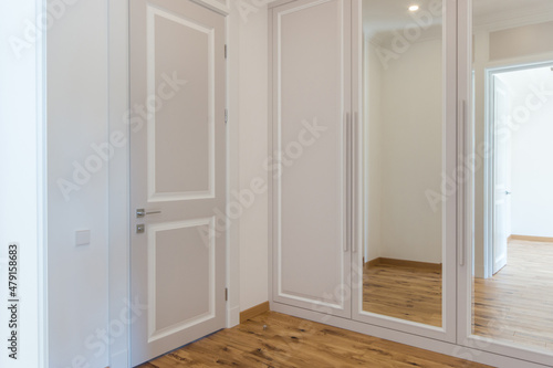 A bright corridor in the house with a door and a mirrored built-in wardrobe.
