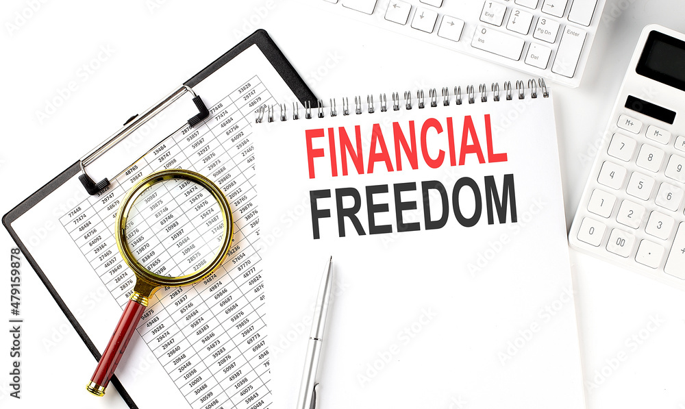 Office desk table with keyboard, notepad ,chart and calculator. Top view with text FINANCIAL FREEDOM Office desk table with keyboard, notepad ,chart and calculator. Top view with text FINANCIAL FREEDOM