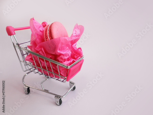 Shopping trolley with macaroons and pink paper wrapping. Gift for March 8th. Valentine's Day. Women's Day. Womens shopping