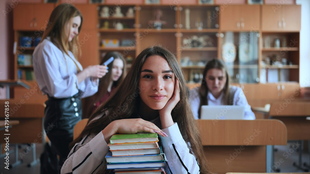 A student poses with textbooks at her desk in her class. A student poses with textbooks at her desk in her class.