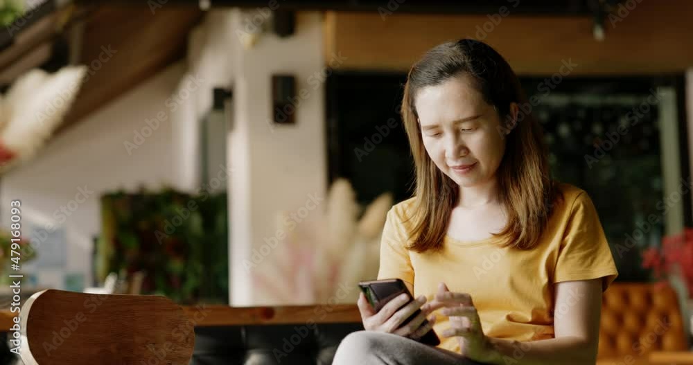 Middle-aged Asian woman sits on smartphone shopping online and order food delivery with great enthusiasm and happiness. Send mobile messages to family with high-speed internet for Free Wifi onsite. Middle-aged Asian woman sits on smartphone shopping online and order food delivery with great enthusiasm and happiness. Send mobile messages to family with high-speed internet for Free Wifi onsite.