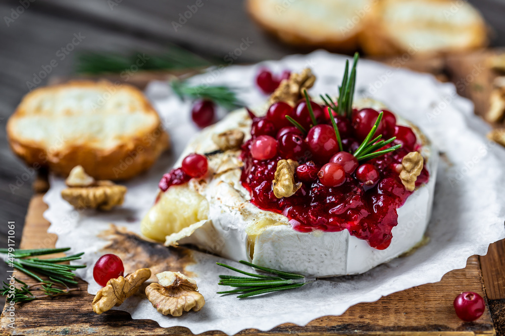 Delicious hot baked camembert with fresh rosemary, cranberry sauce and baguette bread on wooden table. banner, catering menu recipe place for text, top view