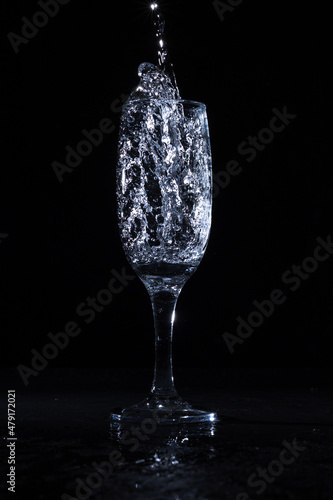 Clear water being poured in translucent goblet placed on table against black background 