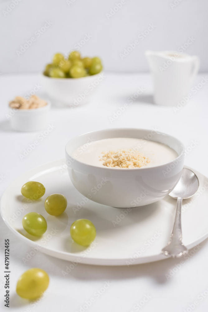 Crema de almendras, sopa fría española. Ajo blanco de Málaga con almendras y uvas en un recipiente blanco sobre una mesa blanca
