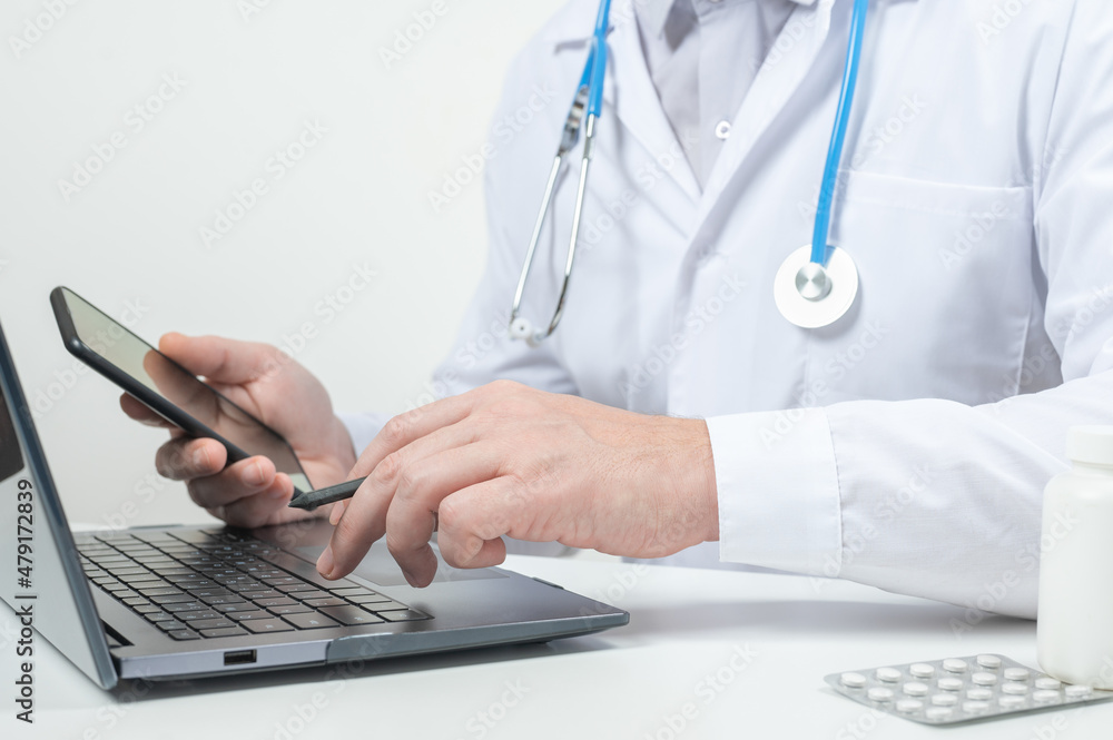 Doctor using laptop for online consultation. Medical doctor working on laptop and phone expanding her medical knowledge further through some online research Doctor using laptop for online consultation. Medical doctor working on laptop and phone expanding her medical knowledge further through some online research