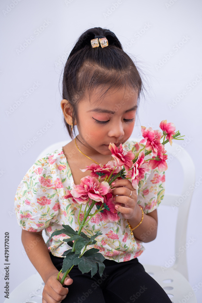 Little adorable asian girl sitting on a white chair, holding flower isolated on white background. Little adorable asian girl sitting on a white chair, holding flower isolated on white background.