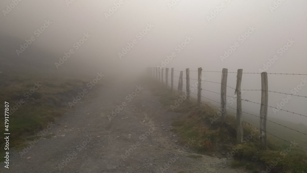 Hiking trail in the fog in the mountains. To the right of the road is the fence