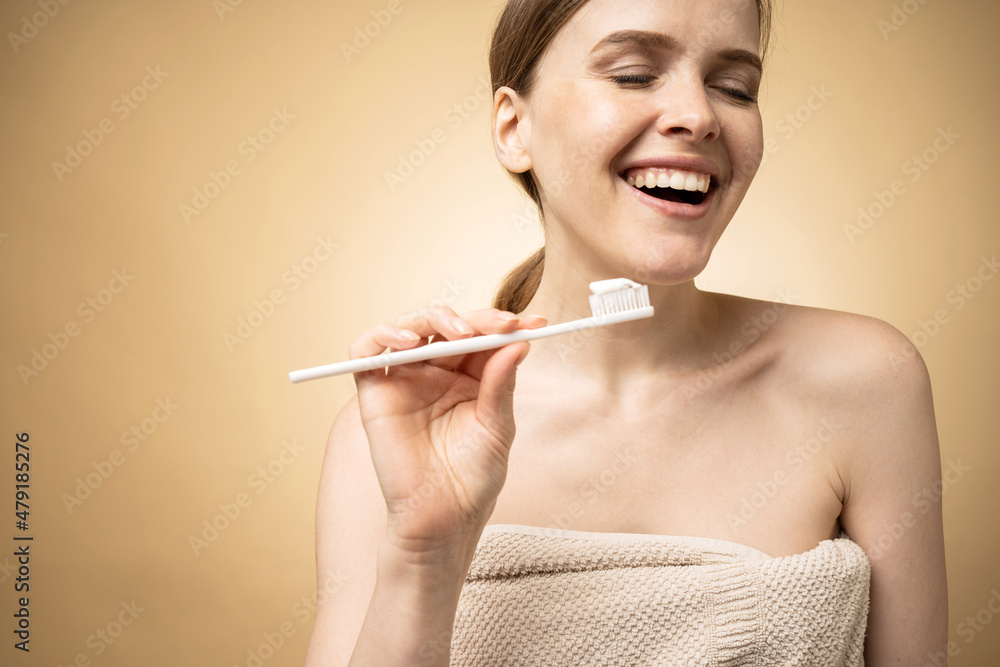Brushing her teeth with a toothbrush and toothpaste, a model woman smiles and shows her teeth in a photo studio Brushing her teeth with a toothbrush and toothpaste, a model woman smiles and shows her teeth in a photo studio