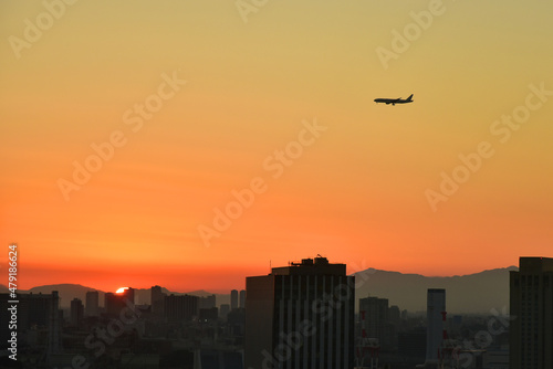 グラデーションになった夕空を背景にした都市と飛行機