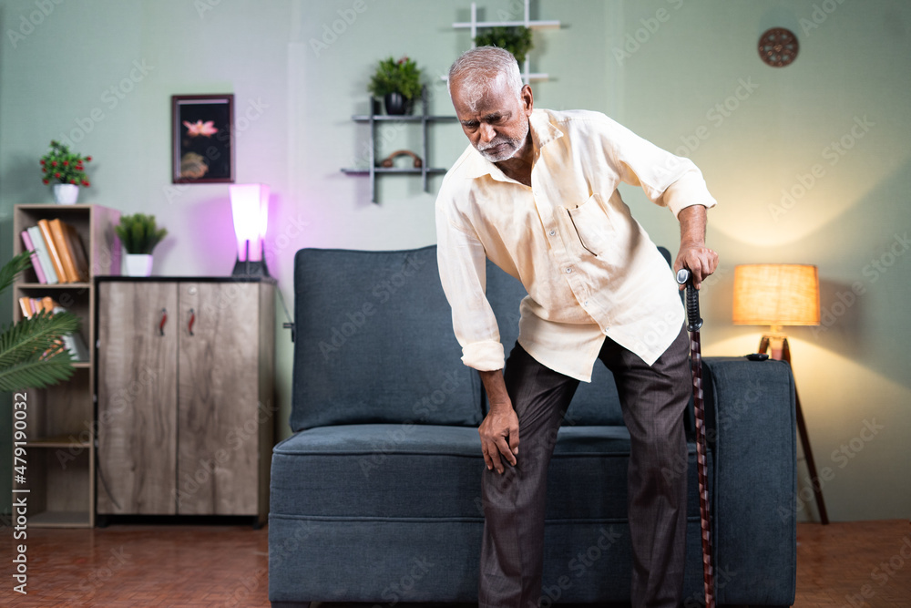 old man trying get up from sofa with support of cane or walking stick