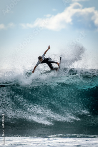 Young surfer with with wetsuit enjoying big waves in Tenerife, Canary Islands. Sporty boy riding his surf board on the ocean wave. Brave teenager making tricks on the rough sea during a competition. © Fabio Principe