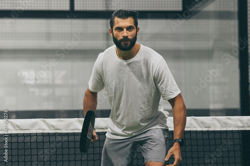 Beautiful man playing paddle tennis, racket in hand   concentrated look. Young sporty boy ready for the match. Focused padel athlete ready to receive the ball. Sport, health, youth and leisure concept photo