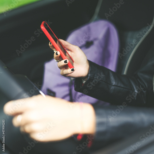 Trendy blonde girl sitting in the car use smartphone. Smiling teen in front of the steering wheel. Young woman enjoying free time wearing black leather jacket driving her car. Youth  teenager concept