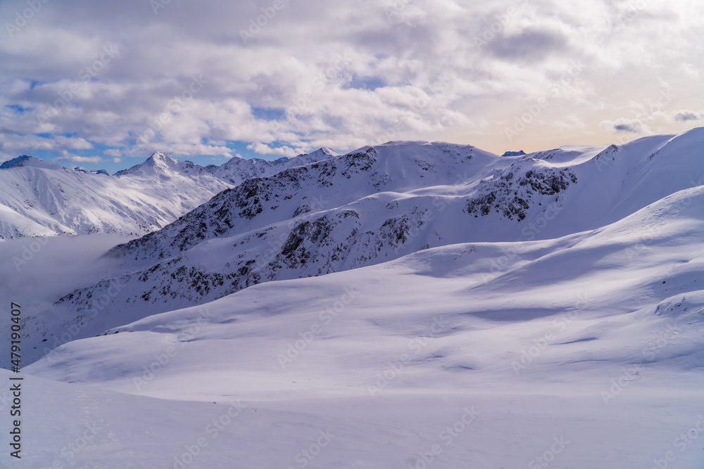 Amazing alpine panoramic sunset view in Livigno, Italy with clouds below snowy peaks