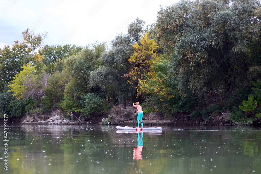 Strong and fit woman rowing with SUP stand up paddle board in Danube river at the summer evening
