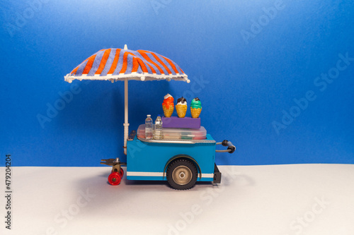 Mini shop ice cream cart with blue red umbrella. Assortment of ice cream. blue wall background. © besjunior