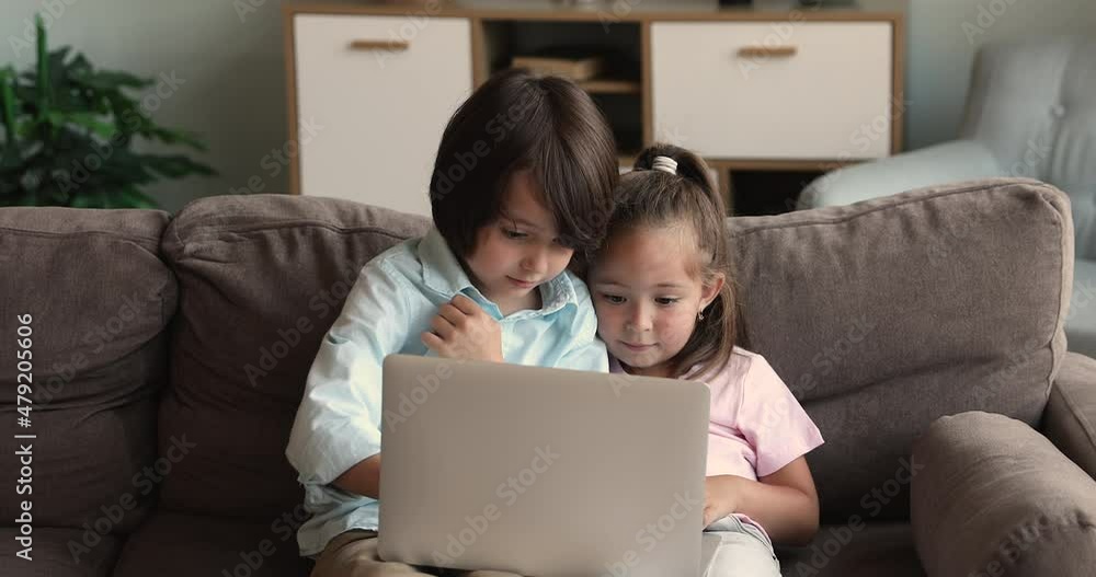 Cute little preschool age children sit on sofa alone using laptop. Smart elder brother teach little sister kid to play online game work in computer app. Parental control software and internet security Cute little preschool age children sit on sofa alone using laptop. Smart elder brother teach little sister kid to play online game work in computer app. Parental control software and internet security