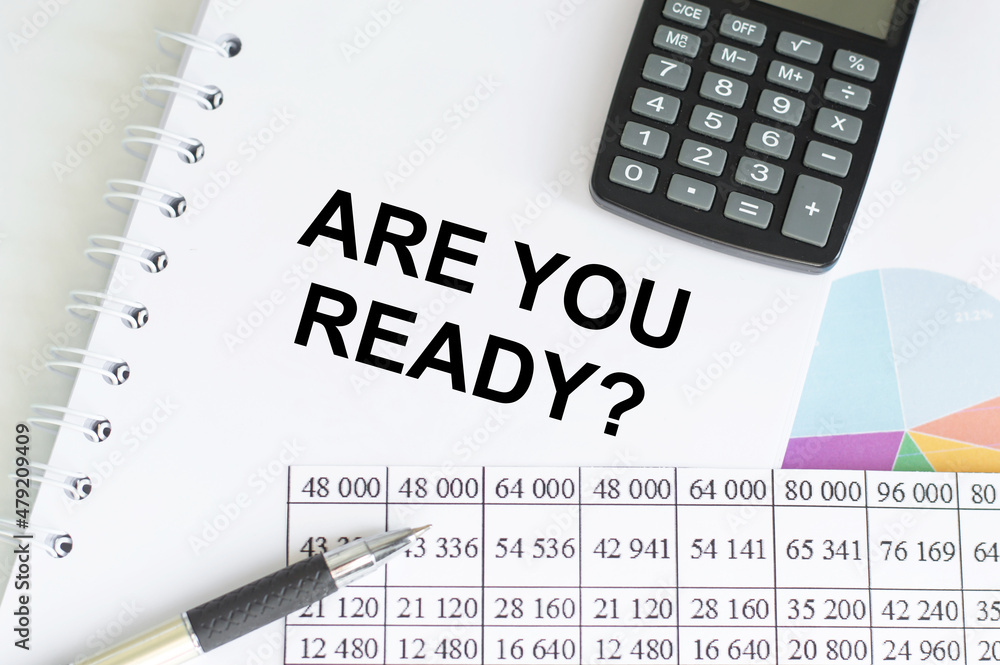 ARE YOU READY text on notebook on the table next to the calculator, pen, graphs with reports ARE YOU READY text on notebook on the table next to the calculator, pen, graphs with reports