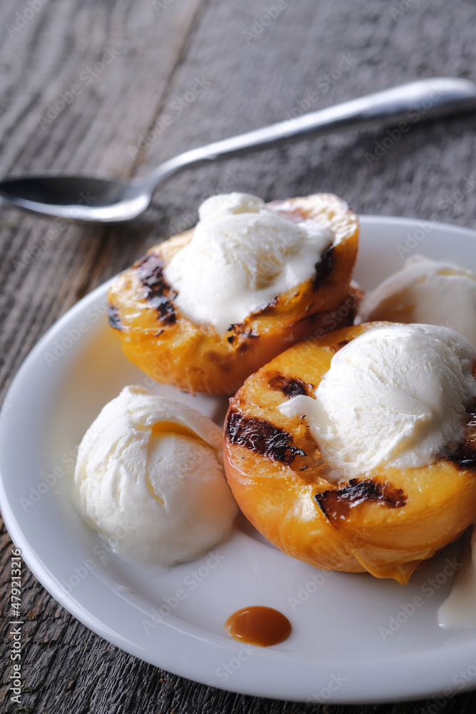 Sweet dessert consisting of vanilla ice cream balls and grilled peach halves and caramel sauce. Wooden grey background.