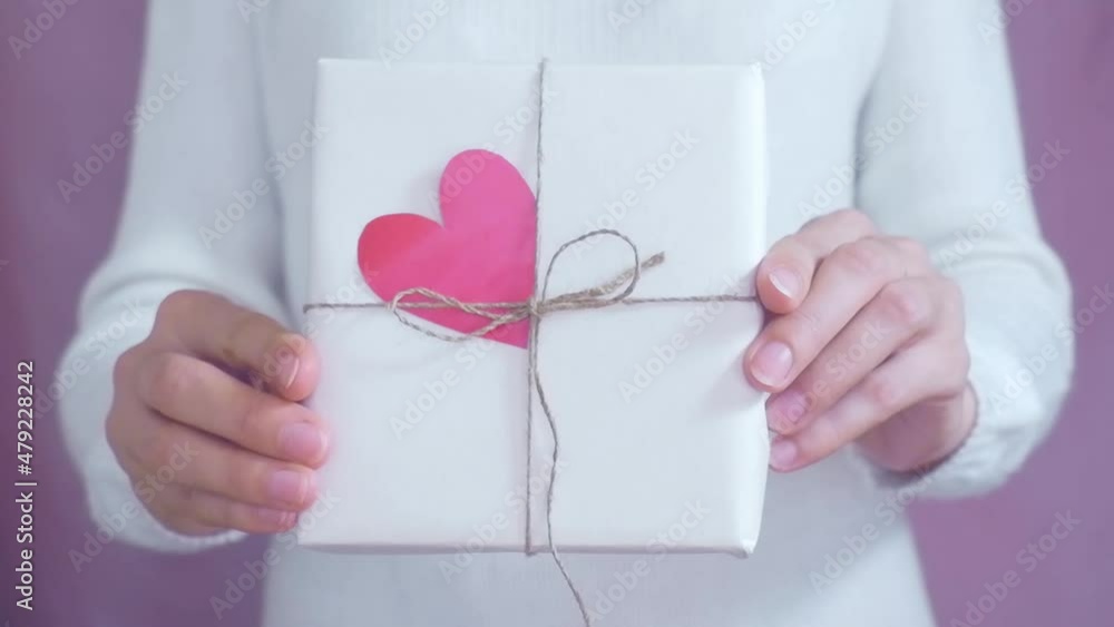 Valentine's day theme. Female hands stretch a gift and a red heart forward towards the camera. Congratulations to the holiday. Selective focus. Valentine's day theme. Female hands stretch a gift and a red heart forward towards the camera. Congratulations to the holiday. Selective focus.