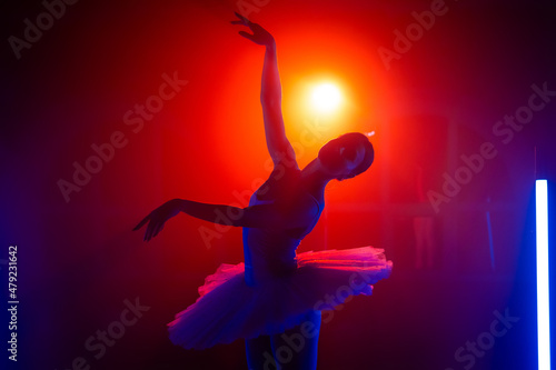 Silhouette of ballerina is practicing elements in studio with neon colorful light. Young woman dancing in classic tutu dress. Gracefulness and tenderness in every movement.