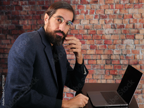 serious man looking at the camera sitting at his desk in front of the computer