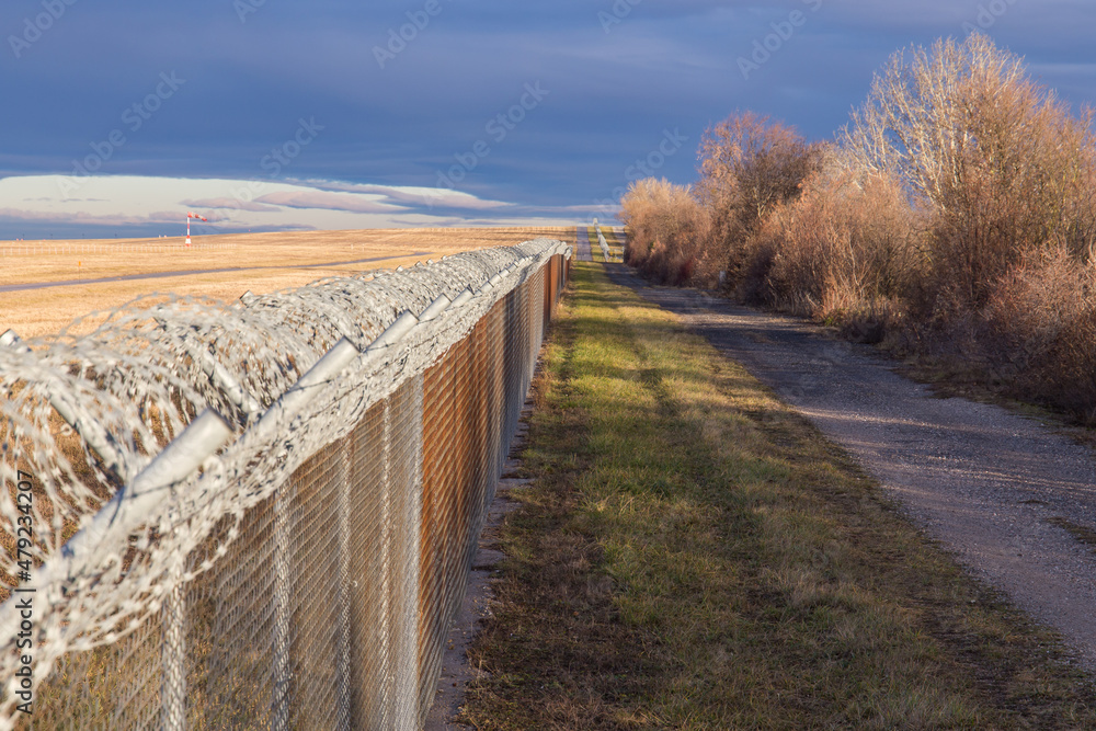 Fence with barbed wire along a state border with dark clouds