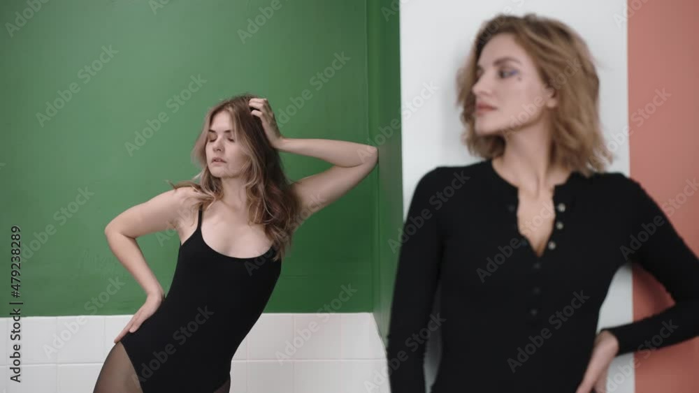 Two blonde women look to the sidestanding in colourful studio. Women in black clothes standing in studio. High quality 4k footage Two blonde women look to the sidestanding in colourful studio. Women in black clothes standing in studio. High quality 4k footage
