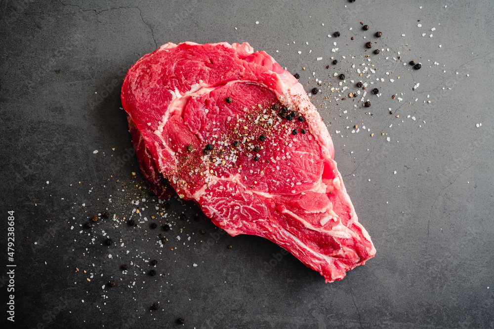 Raw BoneIn Ribeye Steak Seasoned with Kosher Salt and Black Pepper An