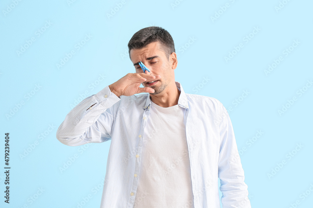 Ill young man with clothespin on his nose against color background