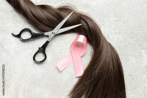 Brunette hair strand for donation with pink ribbon and scissors on grunge background