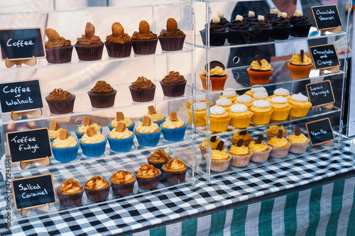 Coffee and walnut cupcakes on sale with other cupcake flavours on glass shelves at an outdoor store