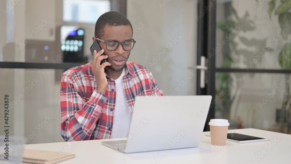 African Man Talking on Smartphone while using Laptop African Man Talking on Smartphone while using Laptop
