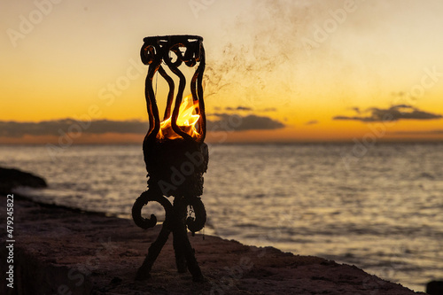 Fire in a Tiki torch burns on a tropical island beach next to the Caribbean sea during sunset.  photo