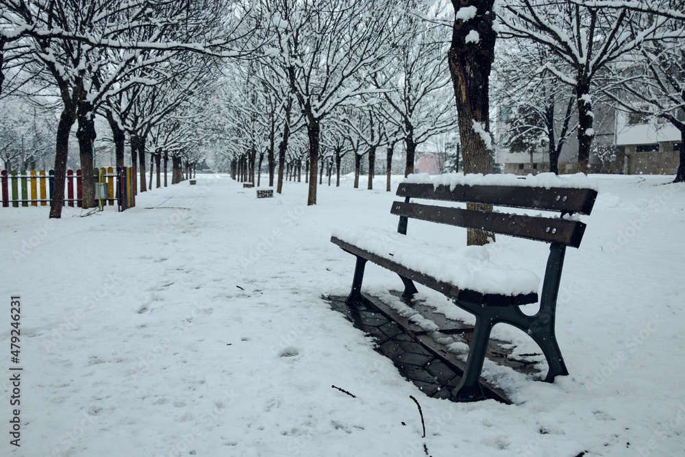 Wooden bench covered in snow in a park in Bulgaria. Snow winter weather. White Christmas. High quality photo